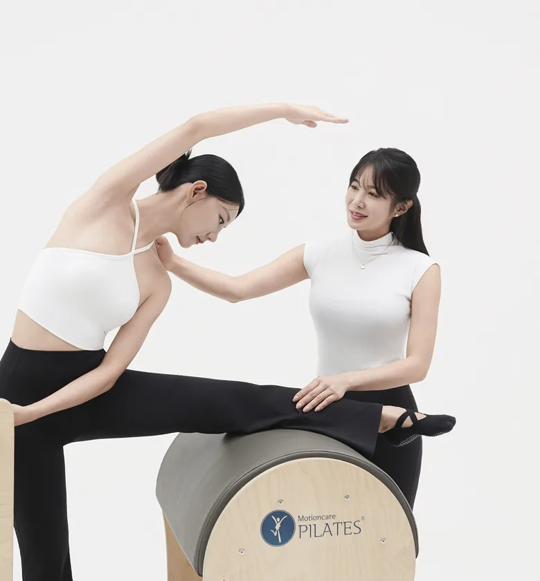 래더 배럴 위에서 회원의 옆구리 스트레칭을 돕는 강사